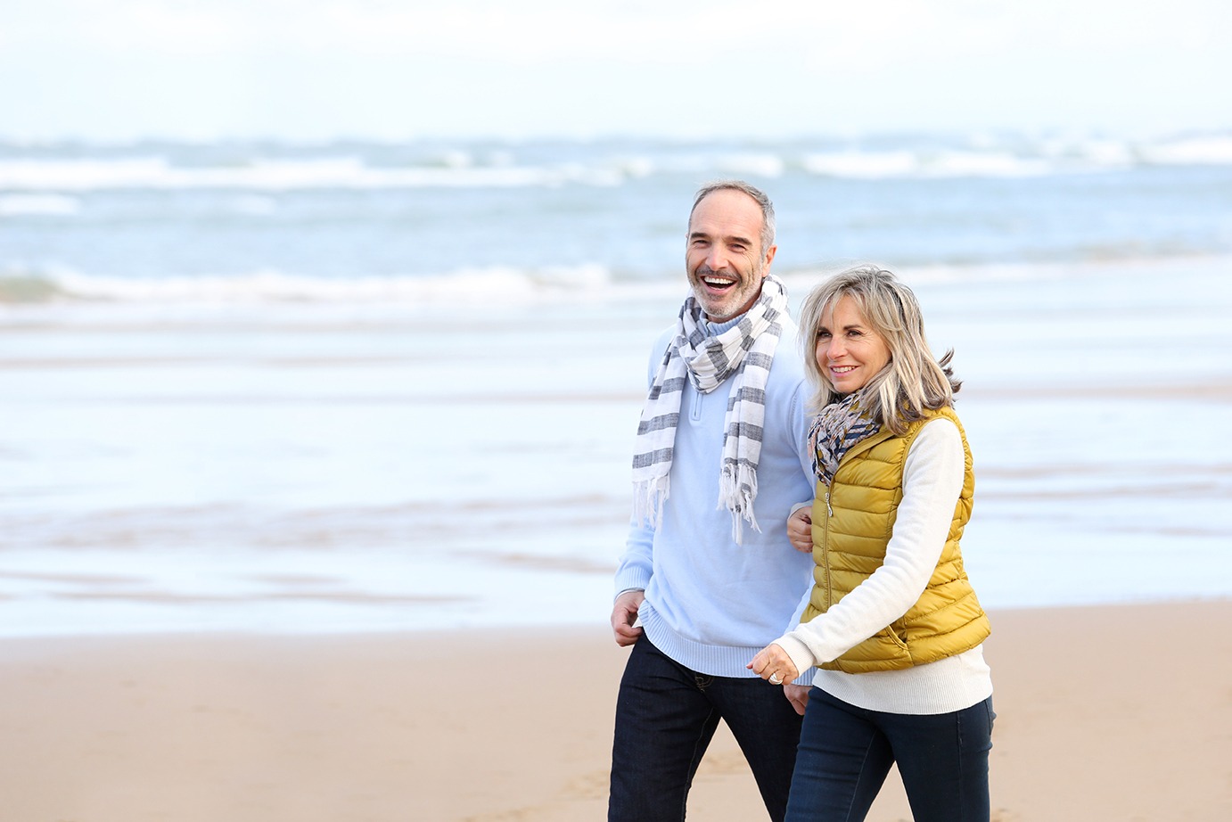 Happy middle aged couple walking on beach on a winter day. Covenant Care.