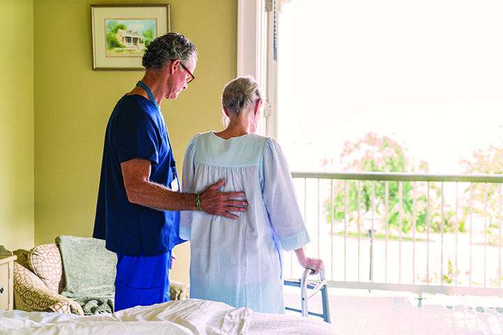 Health care provider assisting an elderly woman in walker. Covenant Care