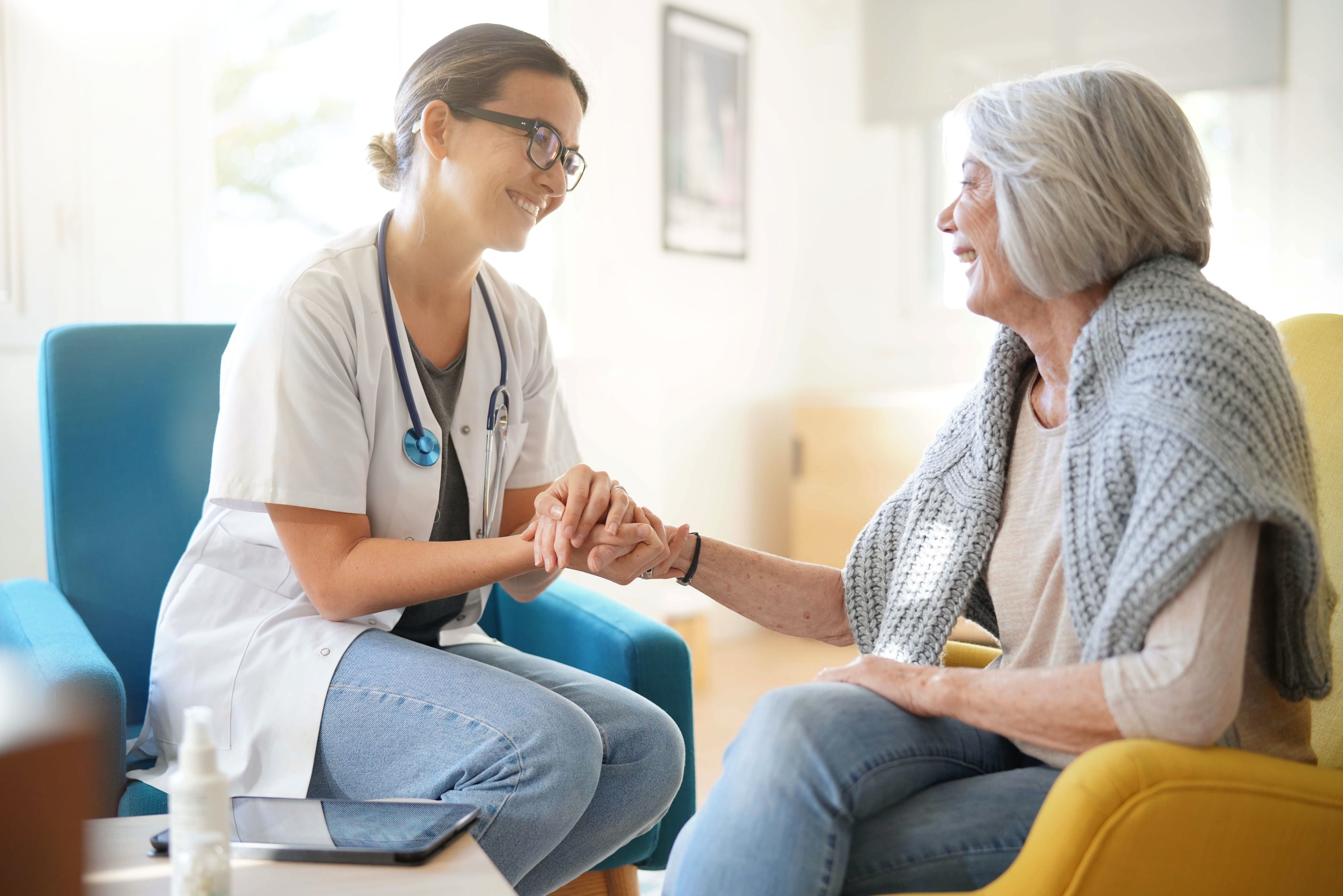 Health care provider smiling and holding hand with elderly lady covenant care