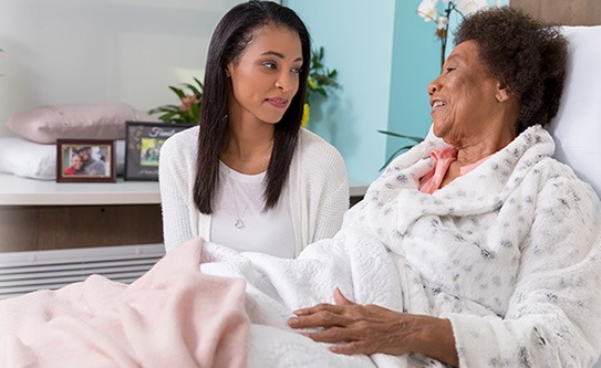 CovenantCare-Inpatient Center-young woman visiting an elderly patient in bed. Covenant Care