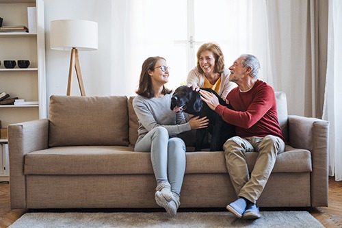 A senior couple with a teenage girl sitting on a sofa with pet dog. Covenant Care