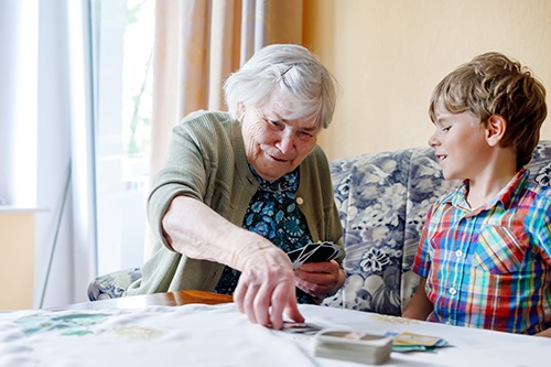 Elderly woman seated at table playing cards with seated young man. Covenant Care