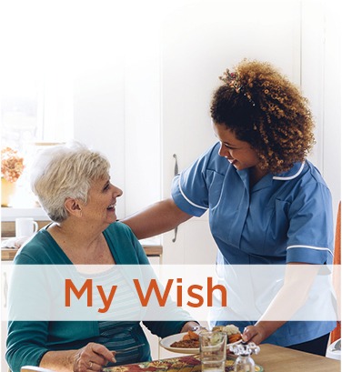 Care giver greeting a seated elderly woman and delivering a plate of food. Covenant Care MyWish